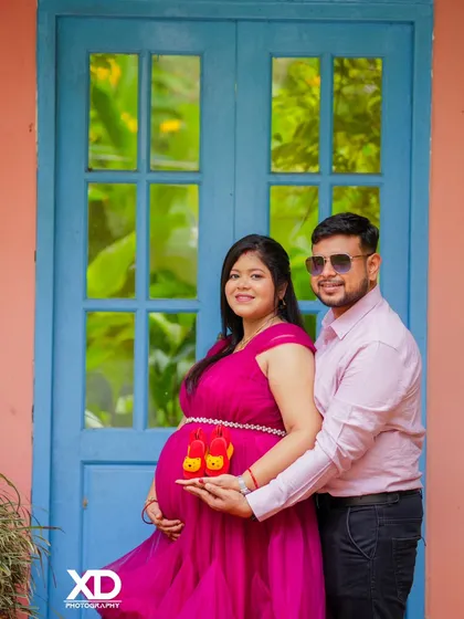 A sweet close-up of a couple holding baby shoes, with a colorful blue door in the background.