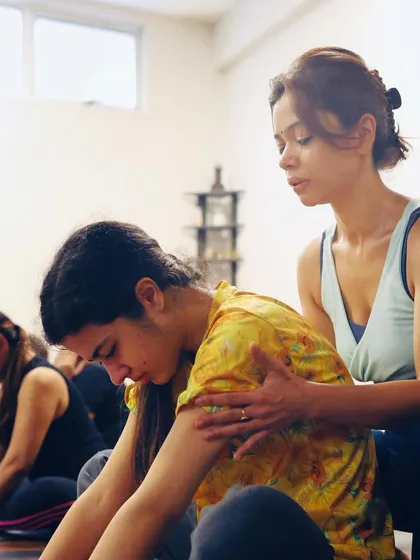Guiding a student in a seated forward bend. My hands on her back encourage her to lengthen her spine and breathe into the space she is creating.
