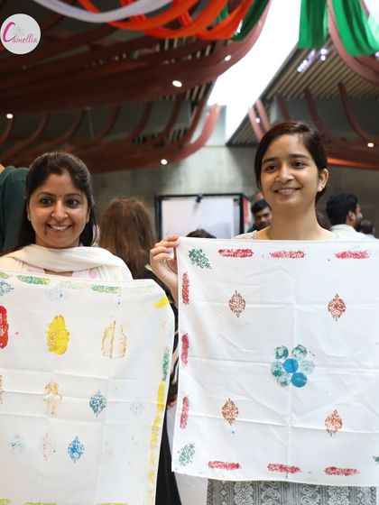 Two women smiling as they hold up their unique, hand-printed textiles. This captures the sense of accomplishment and fun from our creative workshops.