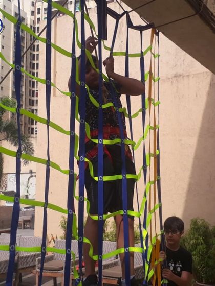 A young student tackles a climbing net, a challenging activity that builds strength and problem-solving skills. We incorporate diverse and fun challenges into our programs.