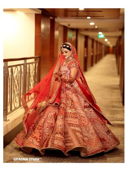 A beautiful full-length shot of the bride in her red lehenga, showcasing the flow of the fabric and the elegance of her posture.
