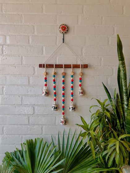 Our 'Beads and Bells' handmade wall hanging in the 'Hibiscus' variant, with red and blue beads. This colorful piece is perfect for adding a vibrant touch to your entrance or balcony.