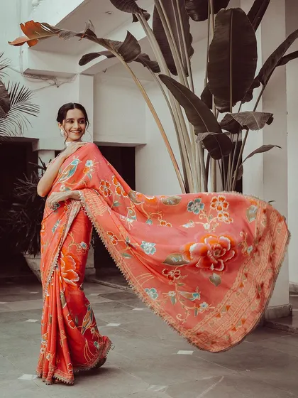 The model shows off the graceful drape of a peach-colored floral saree. The movement in the pallu adds a dynamic element to the photo, while the soft colors are perfect for a subtle, elegant look.