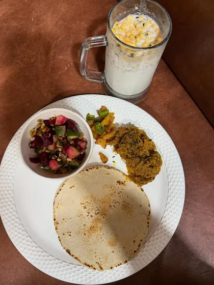 This is my idea of a wholesome meal. It features a balanced plate with a millet roti, a vegetable curry, a fresh salad, and a glass of buttermilk (chaas), covering all the essential food groups.