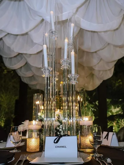 A Chanel-inspired tablescape, featuring tall, modern candelabras, a custom "Chanel" favor box, and a scalloped white ceiling drape.