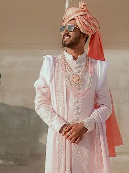 This baby pink Lakhnavi sherwani is a modern take on a classic. Made with a georgette dupatta, it features unique shoulder detailing for a contemporary groom.