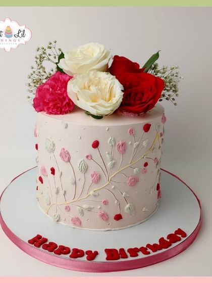 An elegant birthday cake with delicate, hand-piped floral branches and topped with fresh red and white roses.