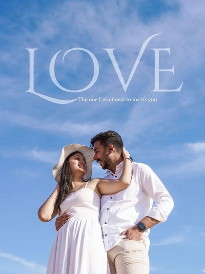 A joyful, bright shot of a couple in all-white outfits against a brilliant blue sky in the desert, with the word "LOVE" elegantly written above them.