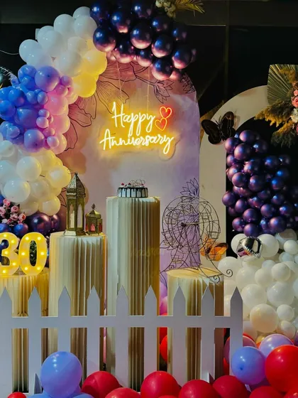 A close-up of the 30th anniversary decor, showing the details of the neon sign, cake pedestals, and lighted marquee numbers. The white picket fence adds a charming touch to the overall design.