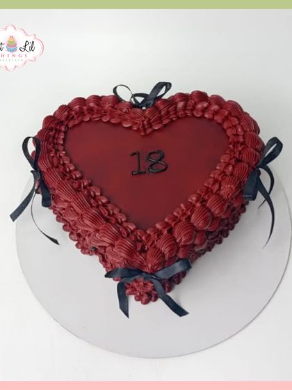 A dramatic heart-shaped cake for an 18th birthday. The deep red is accented with intricate piping and black ribbons for a gothic-romance feel.