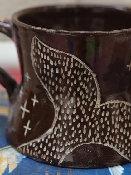 This mug from the 'Lost Marines' set showcases a whale's tail disappearing into a starry sea. The dark coffee-brown clay provides the perfect canvas for the delicate white Mishima lines.