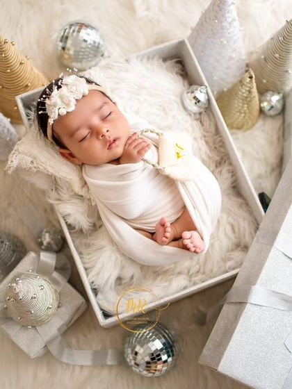 An overhead view of a newborn sleeping in a white gift box, creating a "precious gift" theme for a holiday photoshoot.