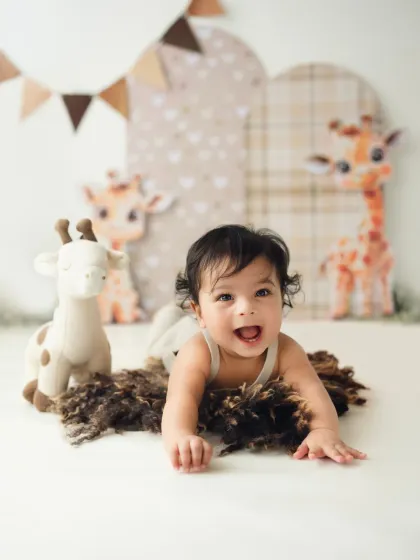 A happy baby on his tummy, enjoying his safari-themed sitter session. His bright smile lights up the photo.