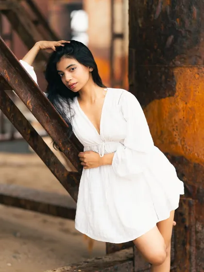 The white dress against the rusty pillar creates a striking visual contrast. It's a blend of softness and roughness, purity and decay.