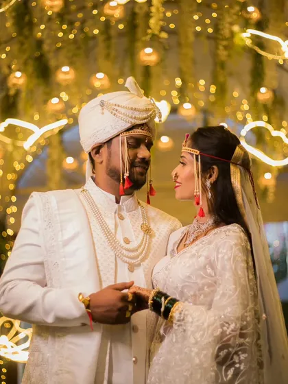 A stunning portrait from a traditional Marathi wedding. The focus here is on the couple's connection, framed by beautiful decor and warm lighting, highlighting the elegance of their coordinated wedding attire and the happiness of the moment.