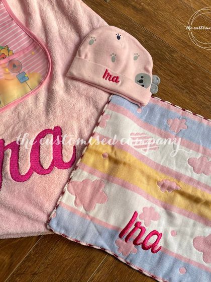 A closer look at the personalized details in our newborn baby set. The name "Ira" is beautifully embroidered in bold pink script on the soft towel, napkin, and cap.