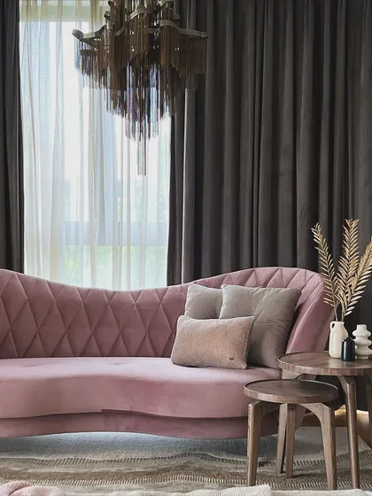 A beautifully styled corner with a plush, curved dusty rose sofa, layered rugs, and a dramatic chandelier, creating a moment of timeless elegance.