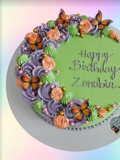A green birthday cake with a crescent of orange, purple, and green flowers, accented with monarch butterflies. The color combination is unique and beautiful.