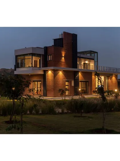 The Nandi Hills residence illuminated at dusk. We used strategic architectural lighting to highlight the building's form and warm brick texture, creating an inviting glow that integrates the home into its natural, grassy surroundings.