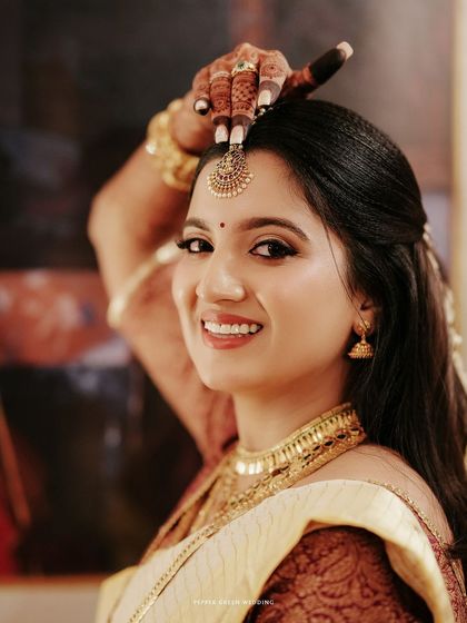 A happy close-up of the bride, her smile bright as she adjusts her maang tikka.