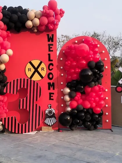A welcome entrance for the Vedsvillie Station third birthday party. The setup includes a custom "Welcome" sign, a large number '3', and railroad crossing signs, all tied together with red and black balloons.