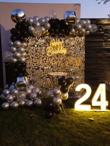 A chic outdoor setup for a 24th birthday, using a silver sequin wall, black and silver balloons, and light-up numbers.