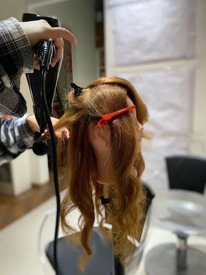 A student practices her blow-drying technique, focusing on creating lift at the root and smoothness through the ends.