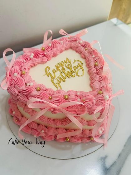 A pretty pink heart-shaped cake with delicate ribbons and gold pearls.