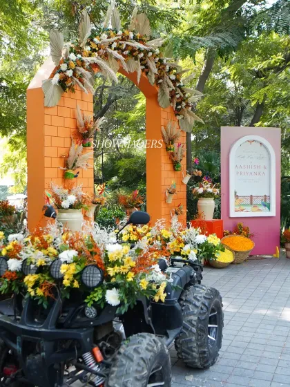 The entrance to the 'Art of Orange' Haldi, featuring a rustic orange brick arch adorned with pampas grass and marigolds, and a flower decked ATV for a fun photo op.