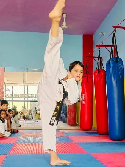 A demonstration of pure flexibility and technique. This student is executing a perfect vertical high kick, a fundamental skill in Taekwondo that requires immense practice and control.