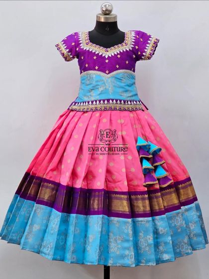 A colorful Pattu Pavadai with a pink skirt featuring a blue border, paired with a light blue and purple blouse.