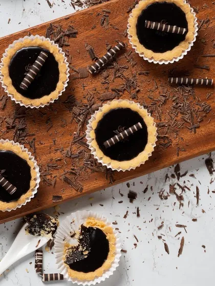 An overhead shot of our mini chocolate tarts, decorated with chocolate curls and shavings. This showcases the clean, elegant presentation of our patisserie selection.