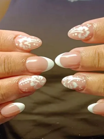 An elegant French manicure with intricate white lace-like patterns painted over the tips of accent nails, adding a delicate, romantic touch.