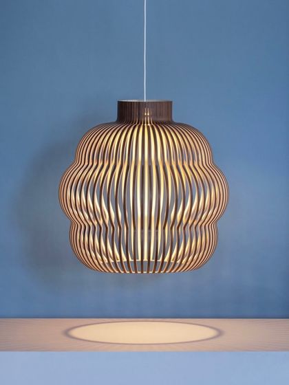 A single Kuulto pendant in a walnut finish hangs against a cool blue wall, its warm wooden tones creating a striking and beautiful contrast.
