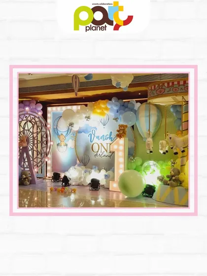 A full view of a whimsical first birthday stage, featuring hot air balloons, a large light-up number one, and adorable teddy bear details.