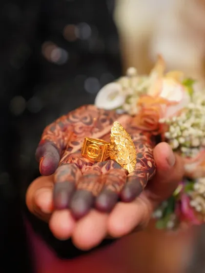 A detailed shot of the wedding rings held in a hand adorned with intricate henna. We believe in capturing the small but significant details, like the rings that symbolize your union, as part of your complete wedding story.