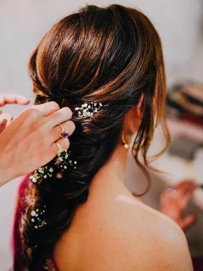 The art of hairstyling. Here, we are adding the final touches of baby's breath to Deepali's intricate fishtail braid, a delicate detail for her Haldi look.
