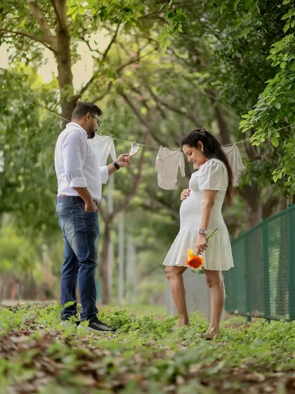 A sweet outdoor scene, getting everything ready for the baby's arrival. Hanging tiny clothes on a line is a creative and heartwarming concept for a maternity shoot.