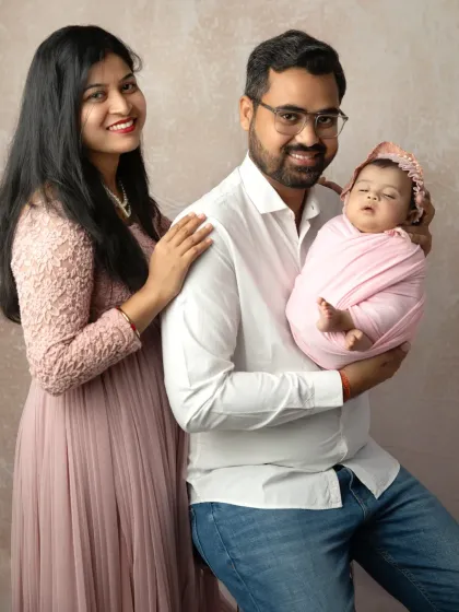 A classic family portrait with a newborn, where the new father stands proudly with his arm around his wife, who is holding their swaddled baby.
