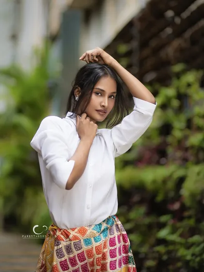A powerful and engaging portrait set against lush greenery. Her pose is confident, and the natural light beautifully illuminates her features, creating a fresh and striking image.