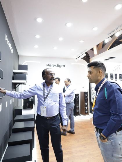 An exhibitor demonstrates the features of a soundbar to an interested couple, showcasing how our platform connects brands with end-users and professional installers alike.