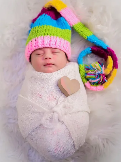 A swaddled newborn wearing a colorful knitted hat, with a small wooden heart placed on their chest. A simple and sweet way to capture newborn love.