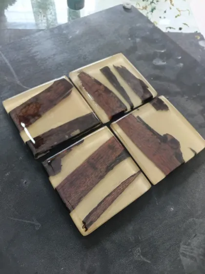 A set of modern coasters where pieces of dark wood are set in a creamy, opaque resin. The clean lines and neutral colors make them suitable for any decor style.