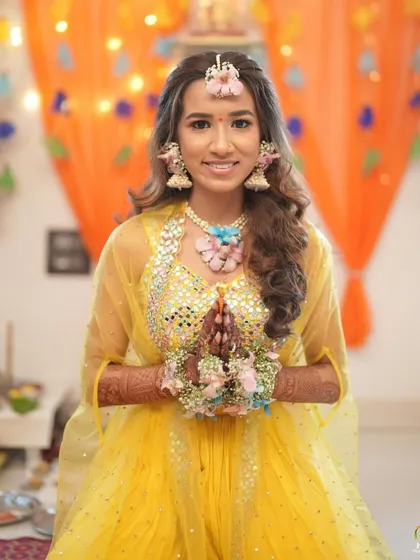 A happy bride-to-be at her Haldi ceremony. We designed this pastel floral set with a mix of pink, blue, and white flowers to match her mirror-work yellow lehenga.