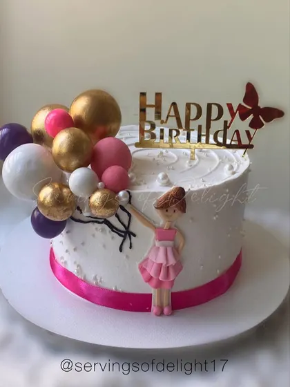 A sweet ballerina-themed cake with a hand-sculpted figurine and a cascade of pink and gold balloon decorations.