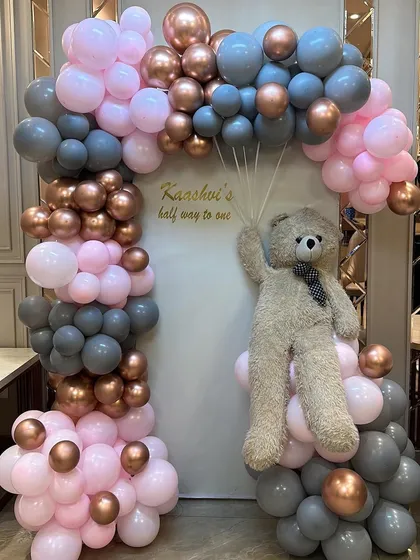 A teddy bear takes flight in this whimsical half-birthday setup. We used a soft color palette of pink, grey, and rose gold balloons to create a gentle and loving atmosphere for baby Kaashvi's celebration.