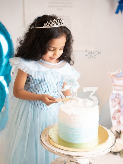 Our little Elsa looks at her cake, ready to make a wish. The tiara and sparkly dress complete her Frozen-themed birthday look.