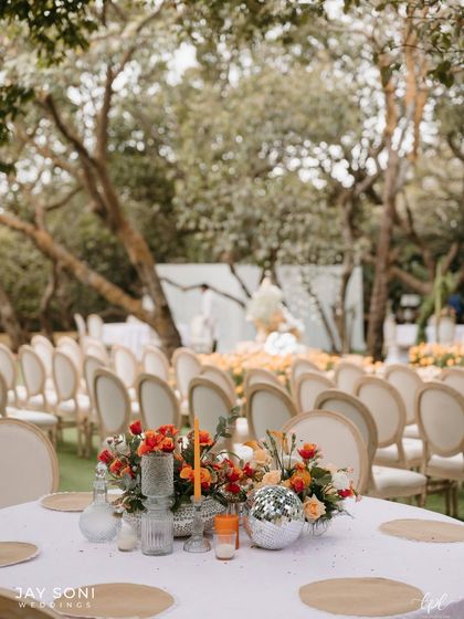 A table centerpiece with orange flowers and a disco ball, looking out towards the ceremony seating, tying all the event spaces together.