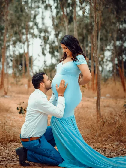 A tender moment as the father-to-be kisses the baby bump during their outdoor session. The soft, natural light adds to the warmth of the scene.