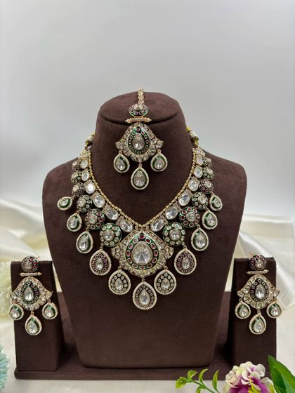 A truly grand bridal set with a distinctive design. This piece features large Moissanite stones and multi-colored Meenakari work, complete with a matching maang tikka and earrings for a majestic look.